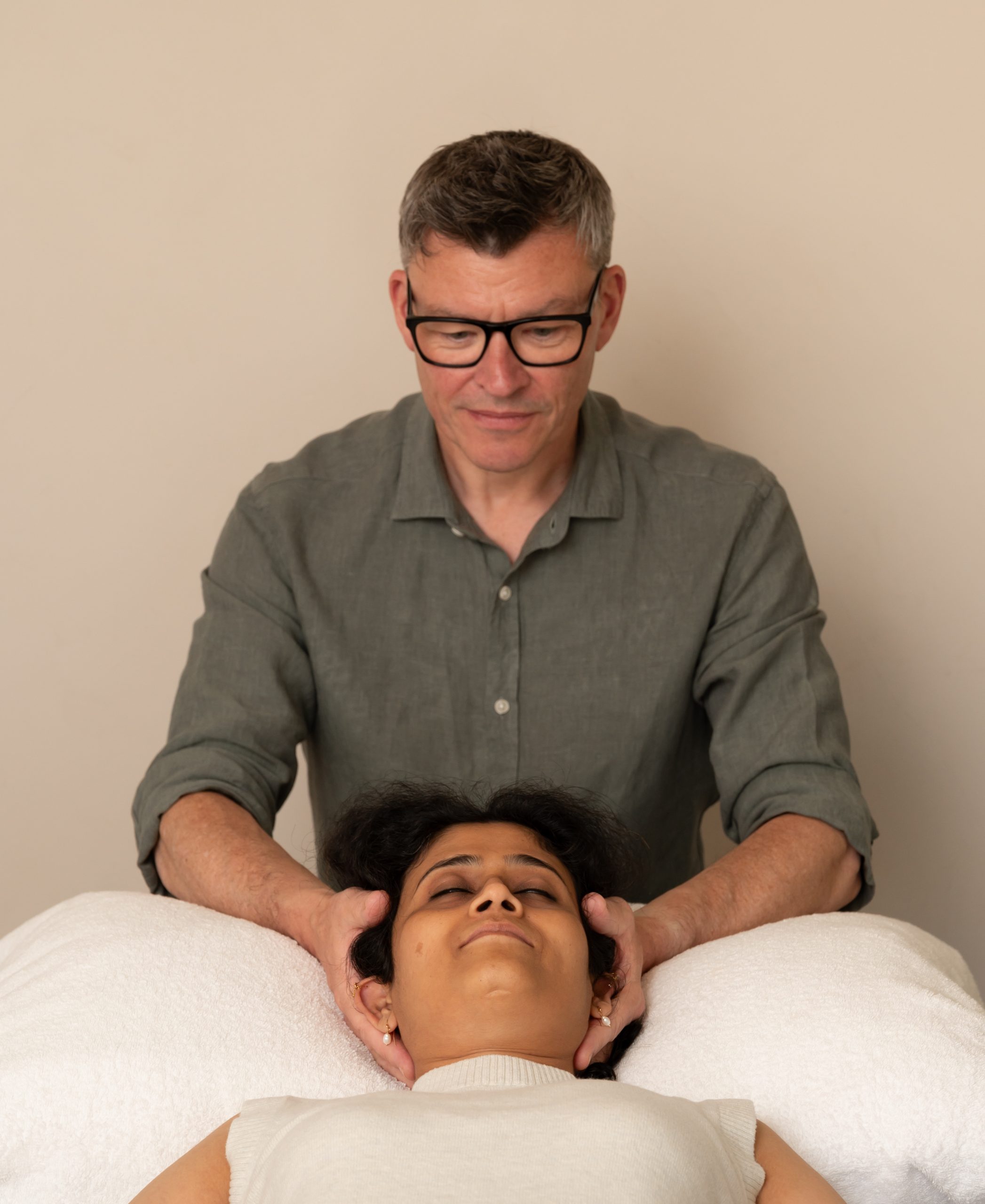 man giving osteopathy treatment to a woman holing her head while the woman is lying on a treatment table
